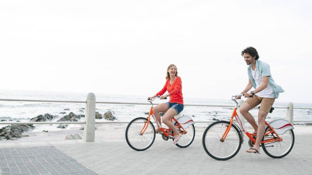 Couple riding bicycle on pavement near promenade at beach